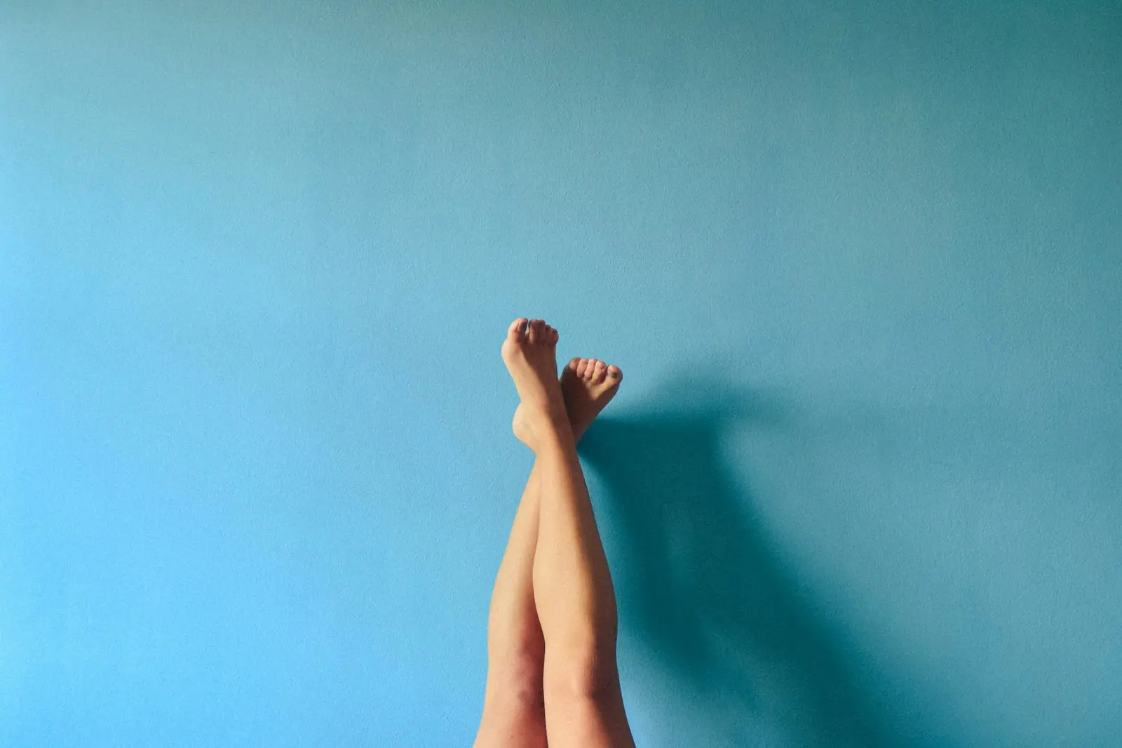 Piernas de una persona apoyadas en una pared turquesa, descalza y relajada